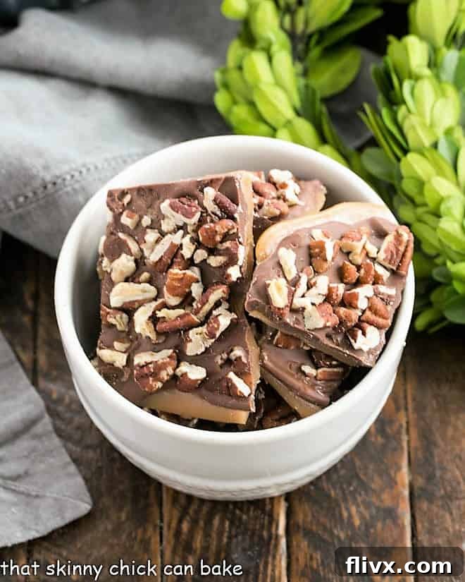 Overhead view of a white bowl filled with glistening Christmas toffee, topped with chocolate and pecans.