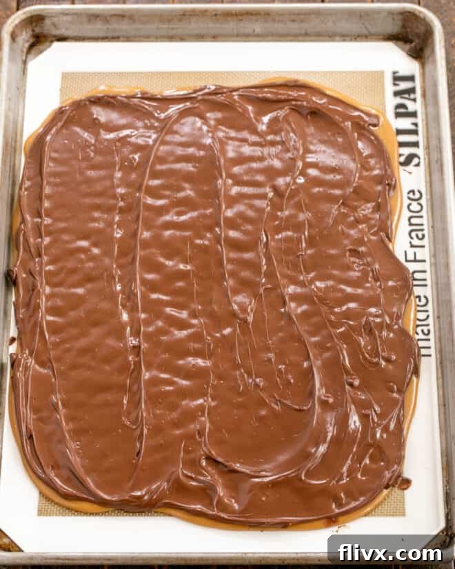 Melted chocolate being smoothly spread across the warm toffee base with a spatula.