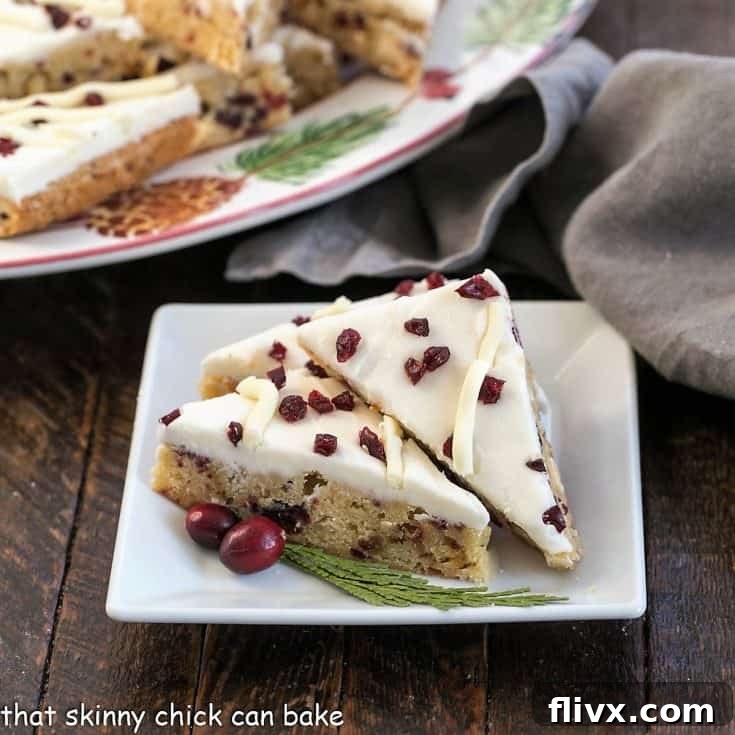 Three cranberry bliss bars on a square white plate with fresh cranberry and cedar garnish