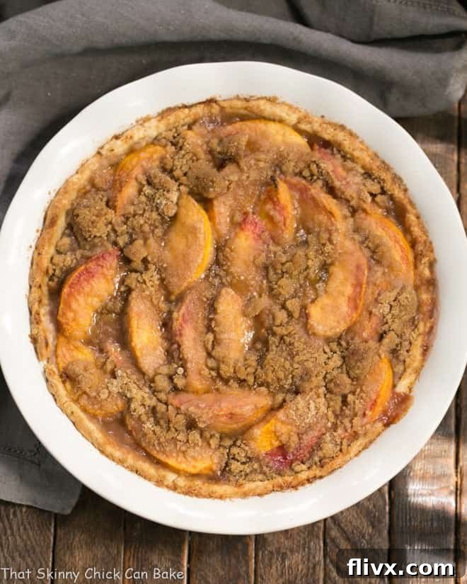 A beautifully baked Easy Peach Crumb Pie, ready to be sliced, set in a white pie plate.
