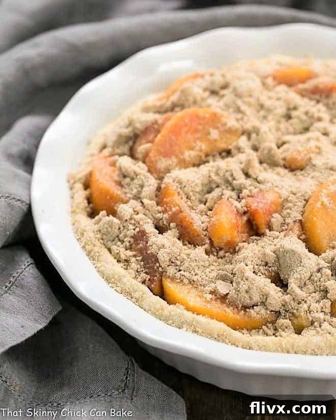 Easy Peach Crumb Pie before baking, showing the arranged sliced peaches and crumb topping in a white pie plate.