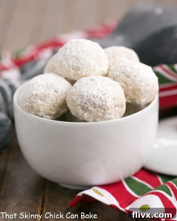 A close-up shot of Pecan Snowball Cookies nestled in a pristine white bowl, showcasing their delicate powdered sugar coating and inviting texture.