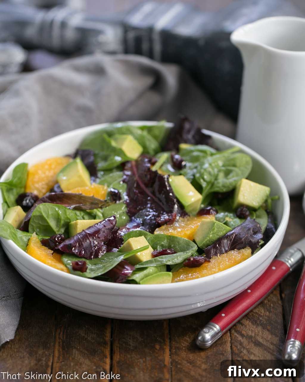 A close-up shot of a refreshing Citrus Spinach Salad with Avocados and Oranges in a pristine white bowl, delicately drizzled with homemade vinaigrette.