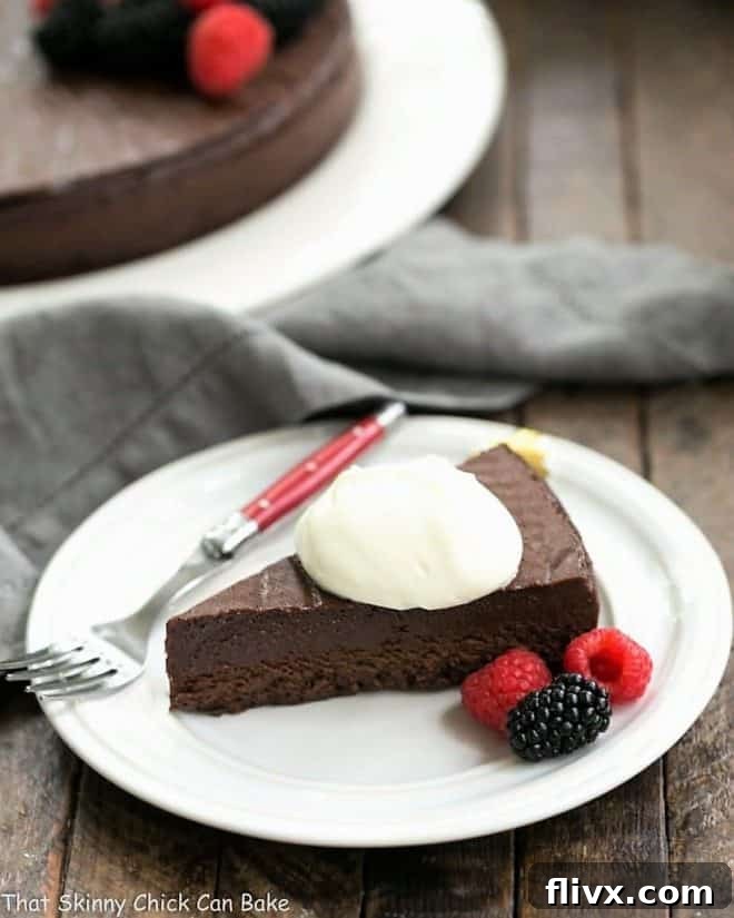 A perfectly portioned slice of Homemade Flourless Chocolate Cake, adorned with a swirl of fresh whipped cream and a single vibrant raspberry, resting elegantly on a round white dessert plate beside a red-handled fork.