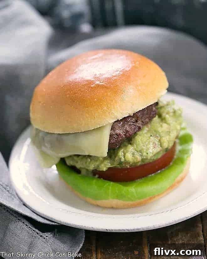 Grilled Guacamole Burger on a round white plate topped with cheese, guacamole, tomato and lettuce
