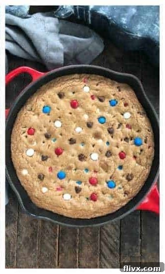 Warm skillet cookie with additional M&M's and chocolate chips being pressed into the surface for garnish.