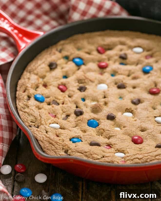 A vibrant Patriotic Skillet Cookie, still in its red cast iron skillet, garnished with red, white, and blue M&M's and chocolate chips, ready to be served.