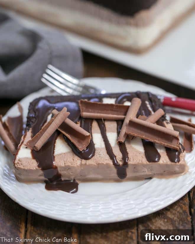A perfectly sliced piece of Homemade No-Churn Ice Cream Cake with Oreo Crust, served on a white dessert plate with a red-handled fork, showing off its distinct chocolate and vanilla layers.