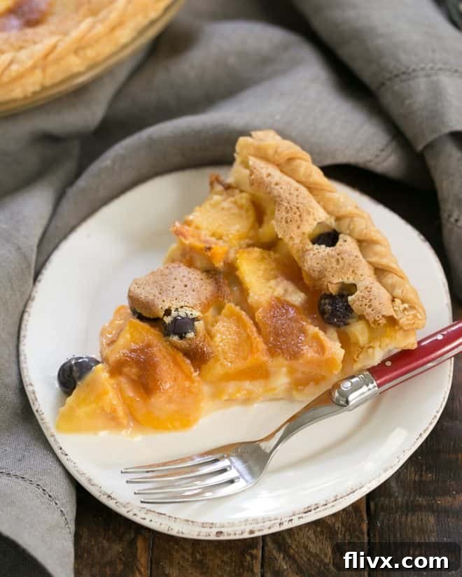 A delectable slice of Blueberry Peach Custard Pie on a pristine white dessert plate, accompanied by a vibrant red-handled fork. The golden crust cradles a luscious filling, studded with bright blueberries and tender peach slices, inviting a taste of summer.