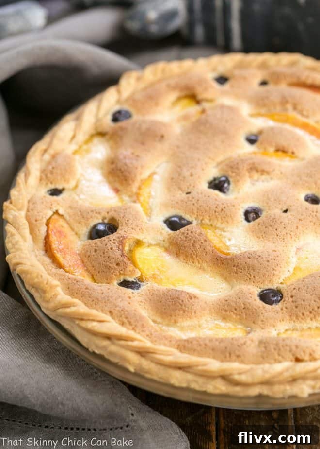 A stunning Blueberry Peach Custard Pie, baked to perfection in a classic glass pie dish, adorned with a beautifully braided crust that adds a touch of rustic charm.
