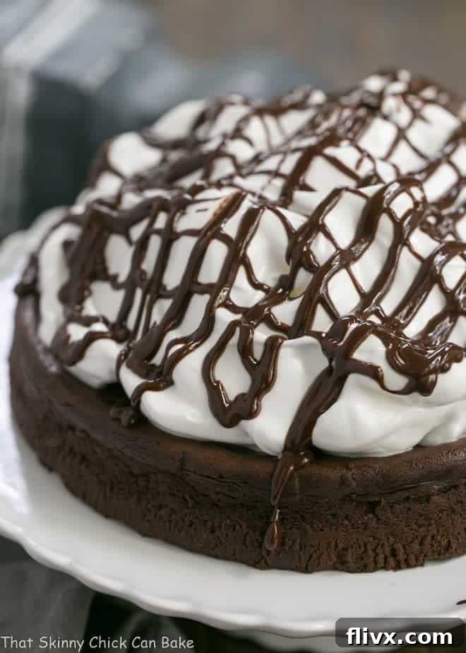 Flourless Chocolate Cake with Marshmallow Frosting on a white cake stand, artfully drizzled with chocolate.