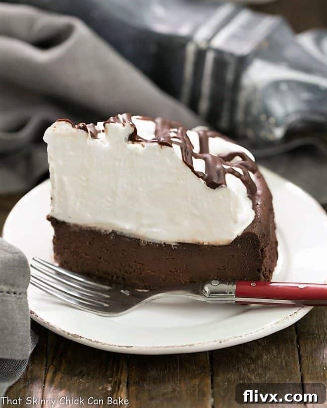 A perfectly portioned slice of Flourless Chocolate Cake with Marshmallow Frosting on a white ceramic plate, ready to be enjoyed with a red-handled fork.