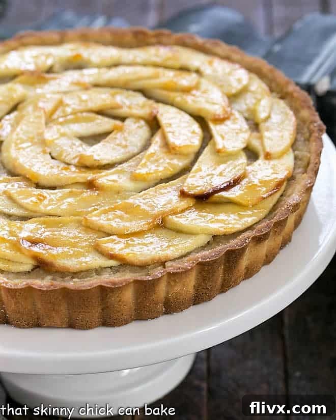 French Apple Tart presented on a pristine white cake stand, showcasing its elegant design.