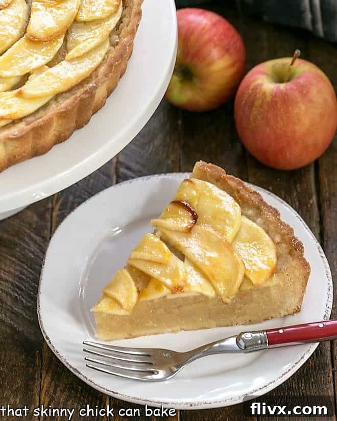 A perfectly sliced piece of French apple tart on a white plate, served with a red-handled fork.