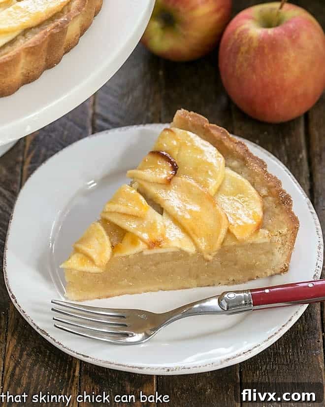 Slice of French apple tart on a round white plate with a golden crust and creamy filling.