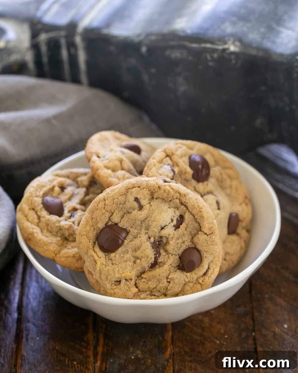 A close-up shot of four golden-brown killer chocolate chip cookies in a pristine white bowl, showcasing their irresistible texture and melted chocolate.