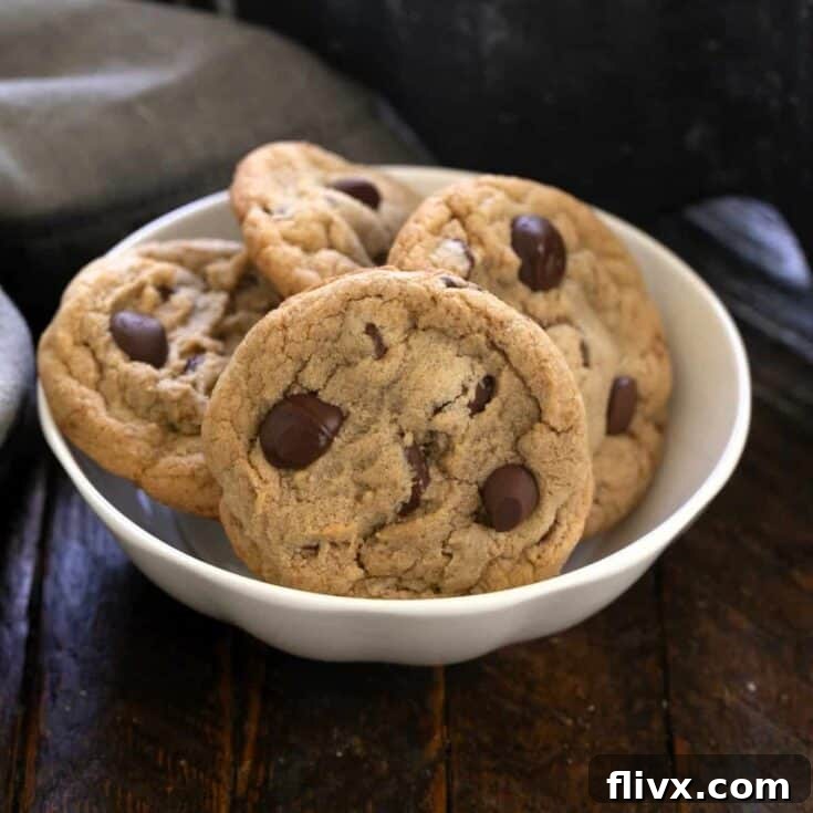 Four golden-brown chocolate chip cookies with melted chocolate, served in a small white bowl, ready to be enjoyed.