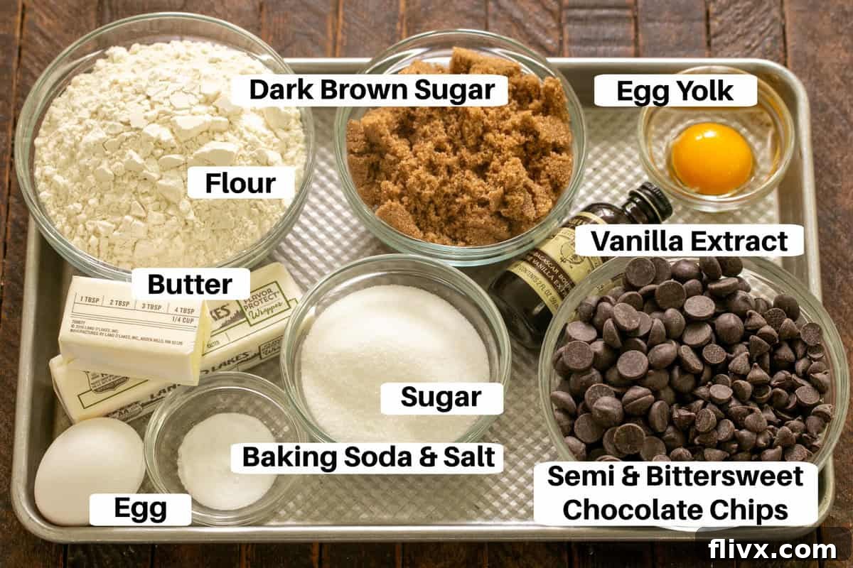 All essential ingredients for killer chocolate chip cookies laid out on a metal sheet pan with labels, including flours, sugars, eggs, butter, vanilla, and two types of chocolate chips.