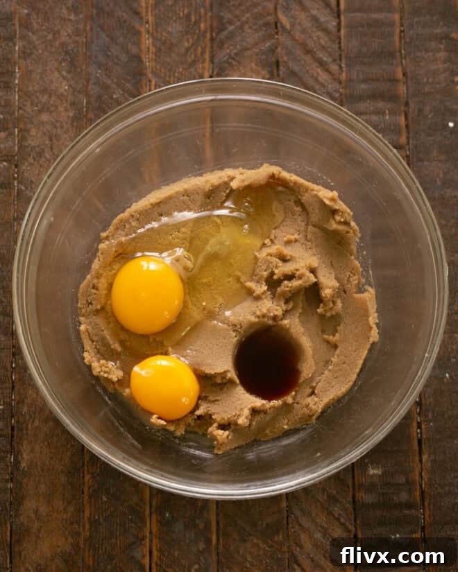 Step 4: Mixing in the pure vanilla extract, whole egg, and extra egg yolk into the creamed butter and sugar mixture.