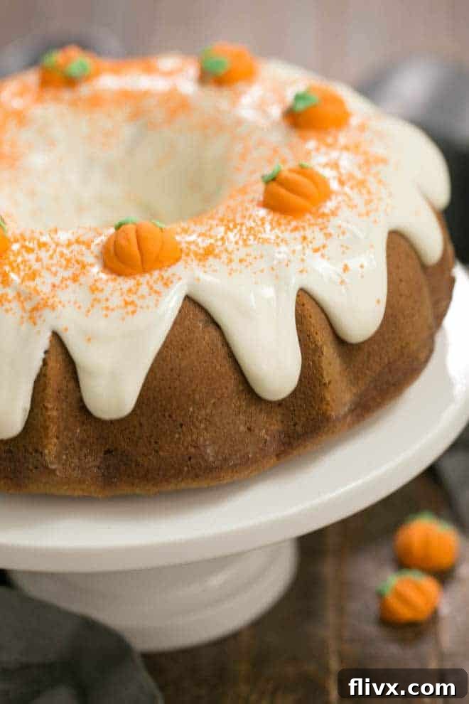 Pumpkin Spice Bundt Cake on a white ceramic cake stand, showcasing its beautiful crown of cream cheese frosting, ready for serving.