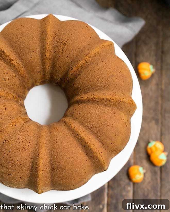 A beautifully frosted Pumpkin Spice Bundt Cake resting on a white cake plate, perfectly baked and ready to be sliced for a fall celebration.