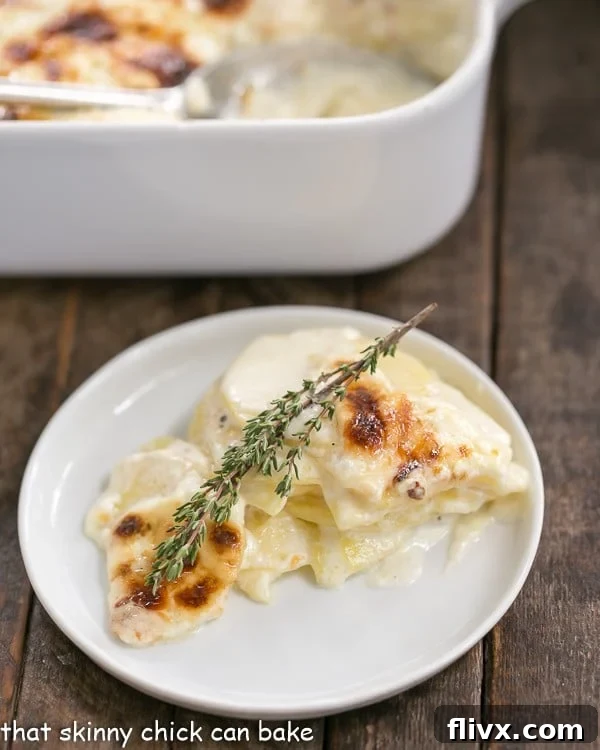A perfectly portioned serving of French Potato Gratin on a small white plate, garnished with a fresh sprig of thyme, showcasing its golden-brown crust and creamy layers.