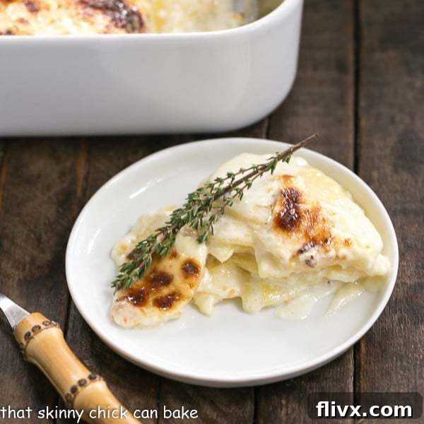 A close-up of a serving of French Potato Gratin on a round white plate, ready to be enjoyed with a bamboo-handled fork, highlighting its creamy layers and golden crust.