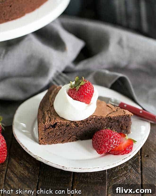 A slice of Italian Flourless Chocolate Cake on a white dessert plate, adorned with a dollop of whipped cream and fresh strawberries, inviting indulgence.