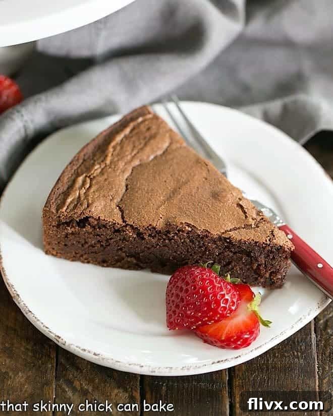A beautifully baked Italian Flourless Chocolate Cake, dusted with powdered sugar and garnished with fresh strawberries, served on a white plate.
