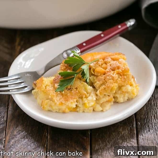Scoop of Jiffy Corn Casserole on a small white plate with a red handled fork, ready to be eaten.