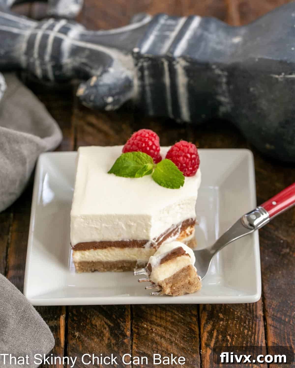 A square slice of Homemade Chocolate Delight on a white plate with a red fork, showing a bite removed from the creamy layers.