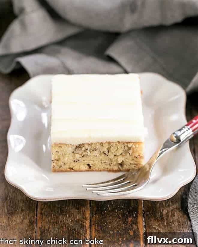 Sour Cream Banana Cake - a tender banana cake topped with a luscious layer of cream cheese frosting! Sour Cream Banana Cake on square ceramic plate, showcasing its moist texture and generous frosting.