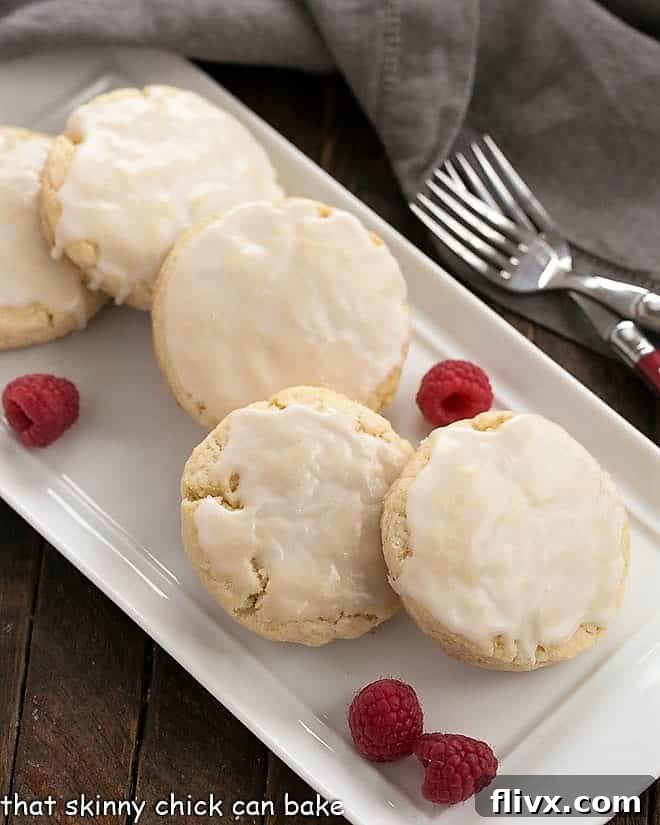 A tray filled with freshly baked, glazed vanilla bean scones, garnished with bright red raspberries, ready for serving.