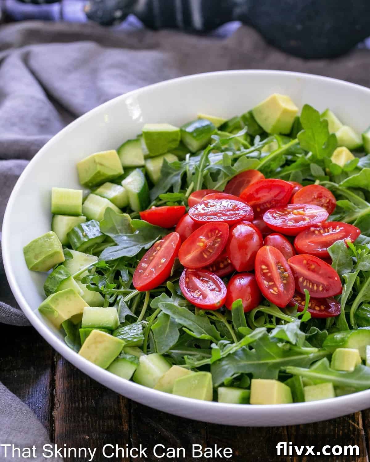 Bright and Peppery Arugula Salad 2 Fresh Arugula Salad with vibrant tomatoes and cucumbers in a pristine white serving bowl, ready to be dressed.