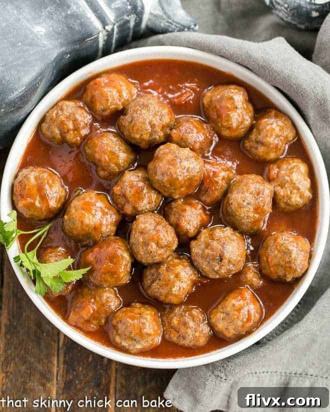 Overhead view of apricot glazed cocktail meatballs in a white serving bowl, garnished with fresh parsley.