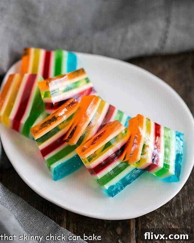 Slices of Layered Jello Rainbow Salad arranged neatly on a white oval dish, showing off its many colorful layers.
