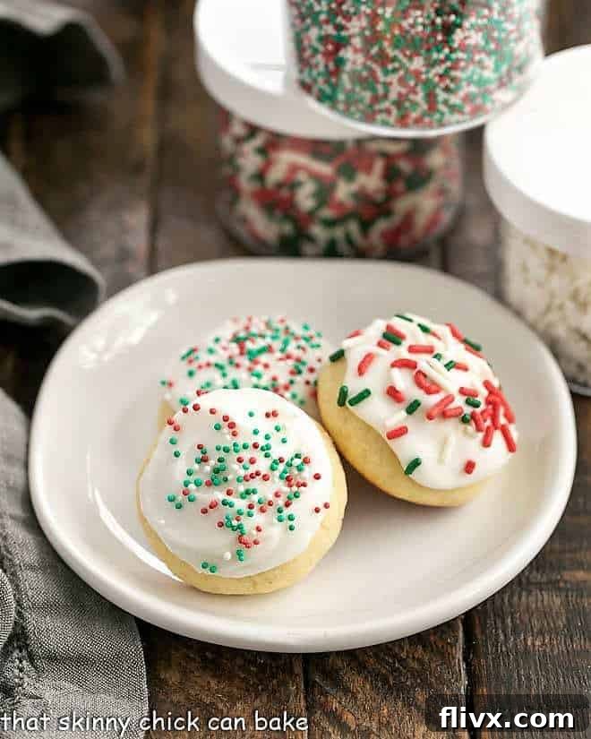 Three soft Italian Ricotta Cookies with white icing and colorful sprinkles on a round white plate, ready for a festive gathering.