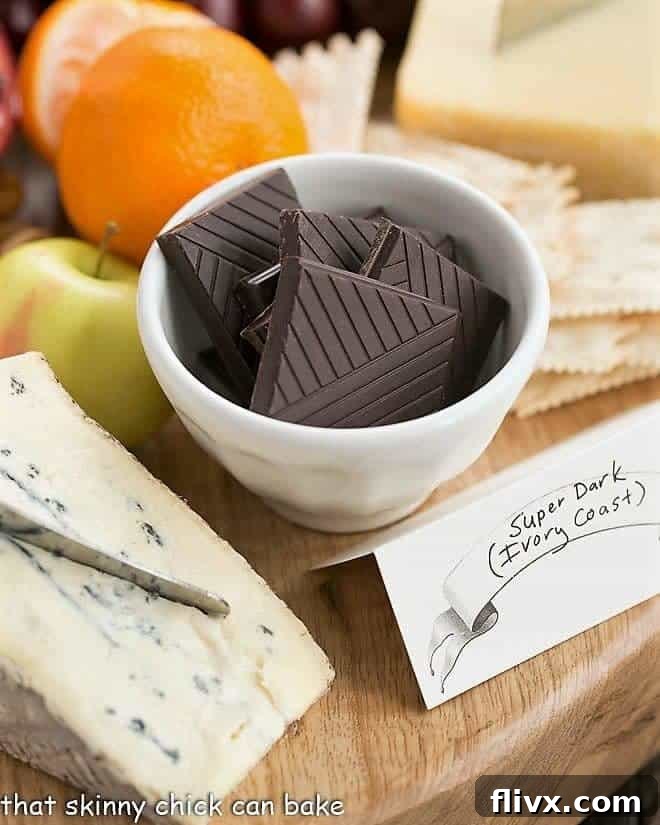 Chocolate Dessert Board - an elegant way to end a meal with top notch chocolates, fruit and cheeses artfully displayed for a jaw dropping presentation! Close-up shot of rich dark chocolate squares in a white bowl, accompanied by a wedge of blue cheese and fresh cherries, highlighting a gourmet pairing.
