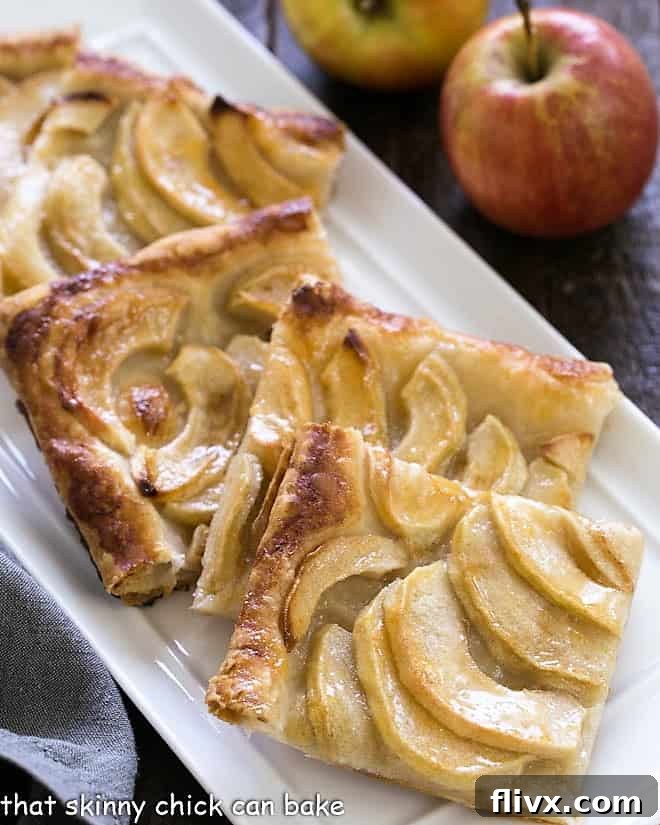 Slices of a golden-brown French Apple Tart arranged artfully on a white ceramic tray, showcasing the delicate apple layers and flaky puff pastry crust.