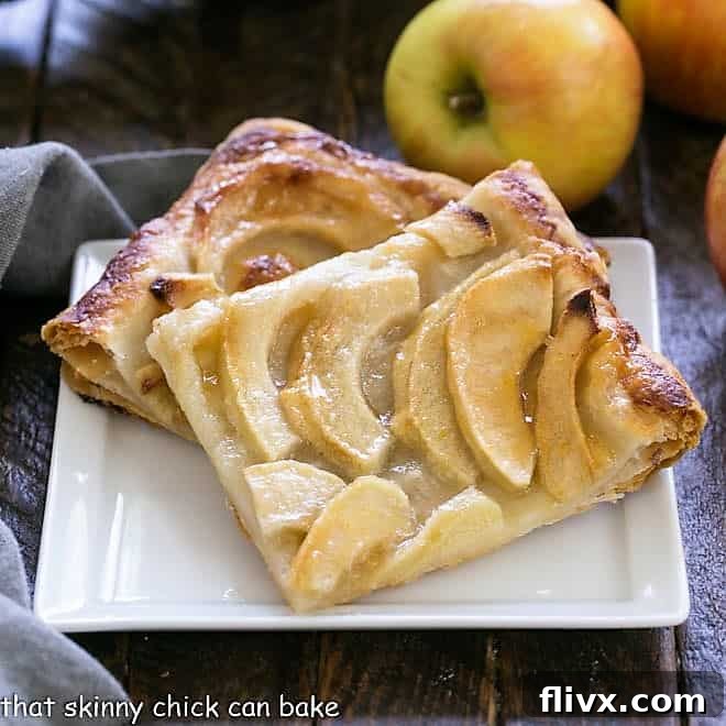 Two slices of a French Apple Tart, beautifully baked and glazed, served on a square white ceramic plate, garnished and ready to eat.