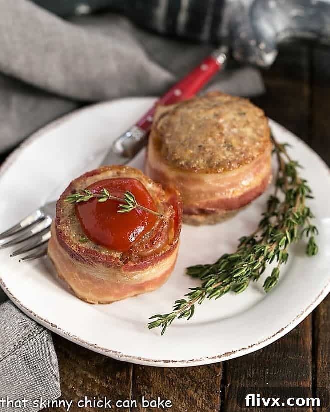 Two bacon wrapped meatloaf muffins on a round white plate, showcasing a unique presentation.