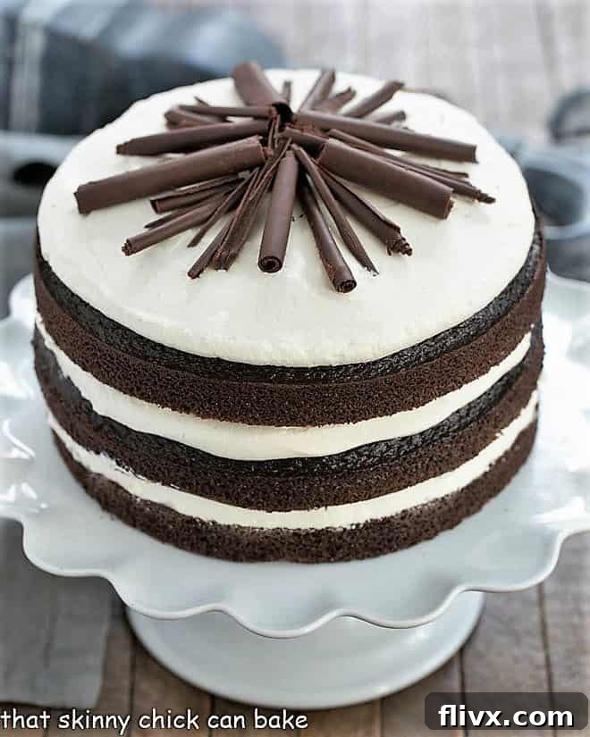 Decadent Triple Layer Chocolate Cake on a white cake stand, richly frosted.