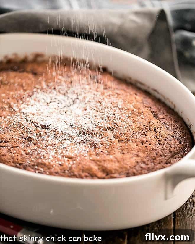 A stunning self-saucing chocolate pudding cake, gently dusted with powdered sugar, resting in an elegant oval casserole dish, ready to be served.