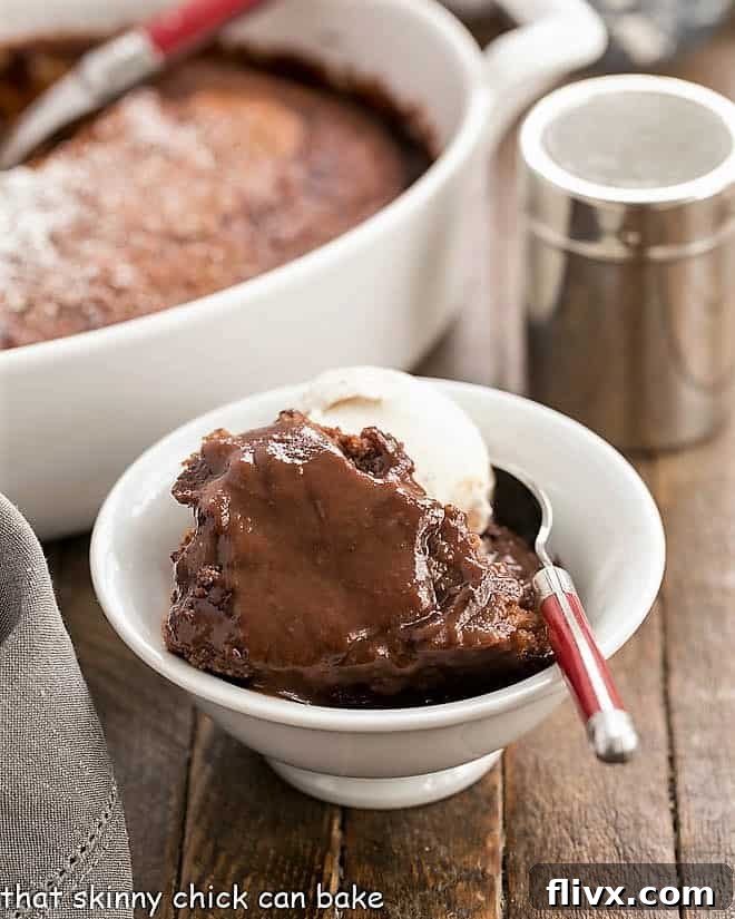 A delectable Easy Chocolate Pudding Cake, perfectly portioned in a bowl, accompanied by a spoon and a scoop of melting ice cream, showcasing its rich, warm sauce.