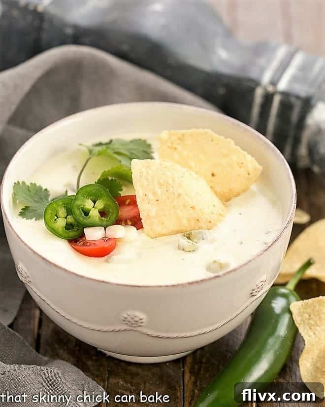 Easy Homemade Queso Dip in a white serving bowl, garnished with crisp tortilla chips, vibrant jalapeno slices, and a fresh sprig of cilantro.