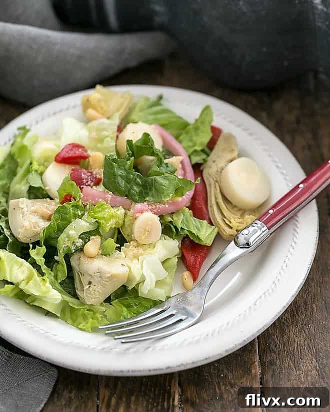 A vibrant Italian Chopped Salad served on a pristine white salad plate, accompanied by a rustic red-handled fork, highlighting the fresh, crisp ingredients and rich dressing.