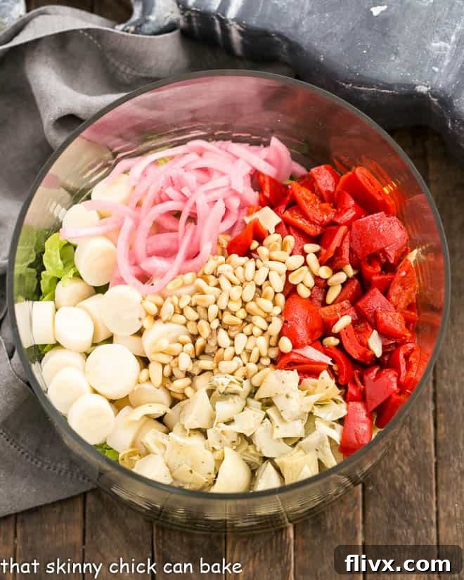 A large glass salad bowl brimming with the colorful, freshly chopped ingredients for an Italian Chopped Salad, showcasing the diverse textures and vibrant hues.