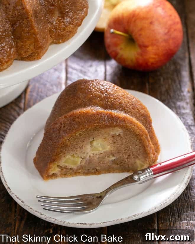 A perfectly portioned slice of our aromatic Apple Bundt Cake, generously laden with chunks of apple and warm spices, presented on a white dessert plate with a red-handled fork, ready to be enjoyed as a delightful autumn treat.