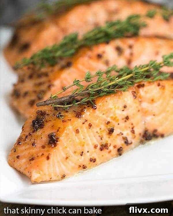 Maple Mustard Glazed Salmon - A super easy glaze, then 15 minutes in the oven for a terrific entree! Two perfectly cooked Maple Mustard Glazed Salmon fillets resting on a white serving tray, garnished with fresh thyme sprigs.