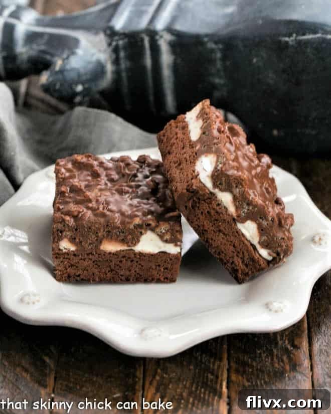 Two perfect slices of Peanut Butter Krispie Brownies showcased on a white plate, highlighting the distinct layers of fudgy brownie, gooey marshmallow, and crunchy peanut butter rice krispie topping.
